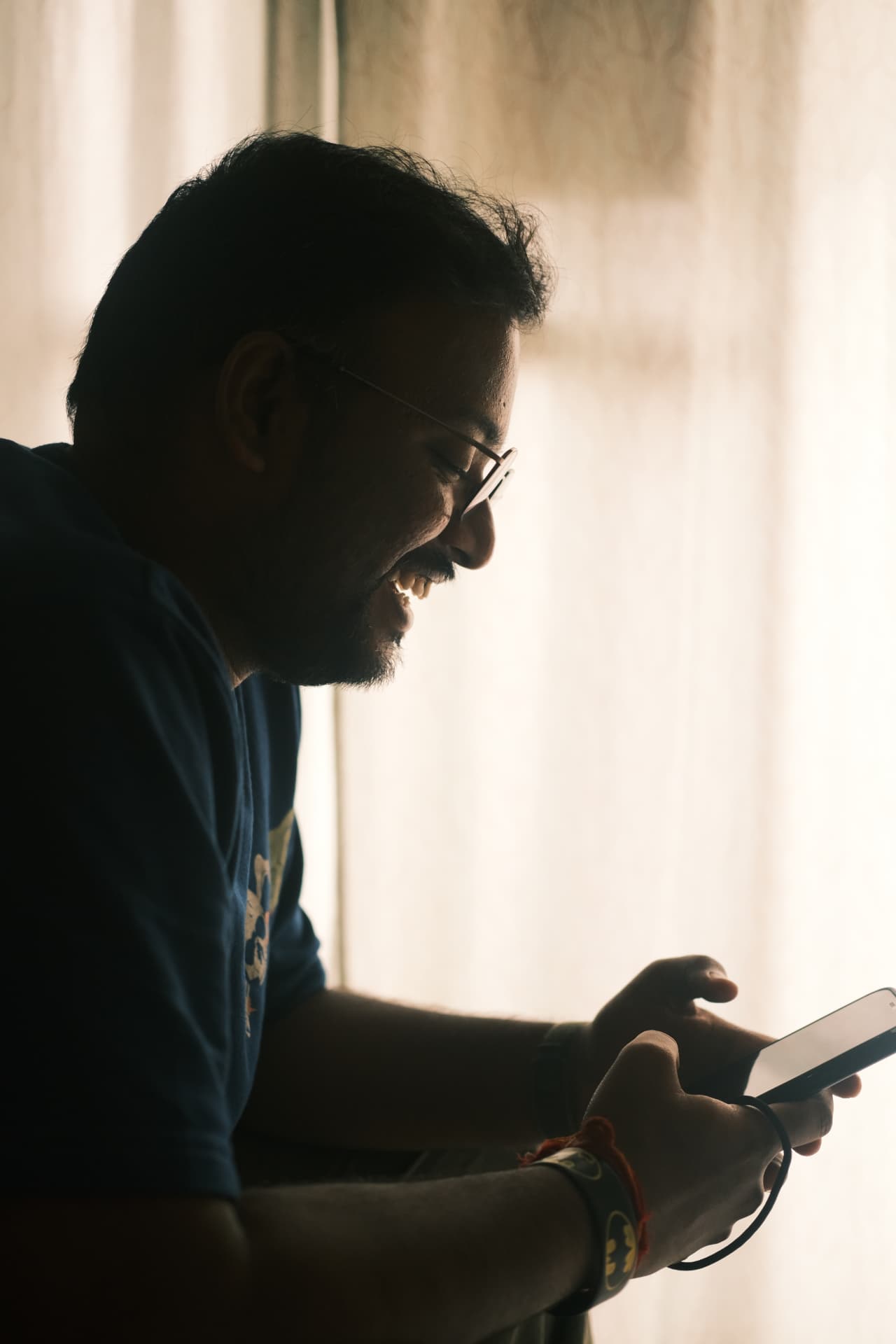 Sreekar Janjirala backlit by a window, laughing at his phone